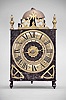 France, Comtoise lantern clock, 8 day, time and strike with alarm, weight driven movement with verge escapement, thread suspension with rear-hanging pendulum in a posted iron frame case, heavy brass chapter ring with Roman numerals, single brass hand, alarm ring with Roman numerals, applied brass spandrels with hearts, all resting on turned iron feet in the front, and topped with a thick pierced brass fronton flanked by two turned brass finials.