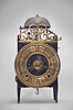 France, Comtoise lantern clock, 8 day, time and strike with alarm, weight driven movement with Chevalier de Bethune escapement, thread suspension with rear-hanging pendulum in a iron posted iron frame, brass chapter ring with engraved Roman numerals, brass alarm ring with engraved Arabic numerals, two iron hands, all surmounted by a cast brass fronton and four turned iron finials.