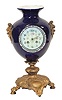 French Urn Clock. Cobalt blue urn is 15 inches high with a gold painted metal base with lions paw feet, and side ornaments that depict mythical lions heads.