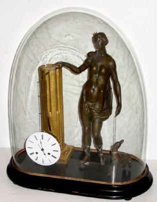 Composite group of clock parts that manage to run. A 1790 rear mount pinwheel movement with 60 pin 'scape wheel, now with associated dial, hands and pendulum rods, suspended from a gilt wood column, flanked by a wooden statue of a lady and dog with 1 broken leg, all under a period glass dome. — Antique Clocks Price Guide