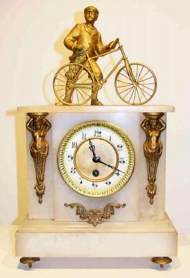 C.1900, French, Man and His Bicycle, atop a white alabaster case, with an 8-day time only pendulum movement, and with a porcelain dial with gilt brass center and case adornments. — Antique Clocks Price Guide