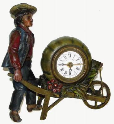 C.1900, French, A spelter novelty of a young farmer pushing a wheelbarrow containing garden vegetables, but notably a large squash which contains a 30 hour alarm clock. — Antique Clocks Price Guide