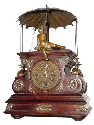 C.1890, German, Rare Flying Pendulum timepiece, a walnut and walnut stained case with lots of cast brass trim, a child at the top with outstretched hand trying to catch the flying ball at the end of the pendulum, the arm and string concealed beneath the umbrella and adding to the eye appeal of the clock. — Antique Clocks Price Guide
