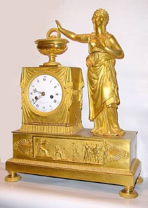 C.1810, French, Barancourt, Ormolu Figural clock, 8-day time and strike, the goddess Athena in a pensive pose. The frieze below the clock with court scene, a gowned lady pleading for mercy from a king with outstretched arm and lancet, a branding fire smoldering behind her, and three warriors with shields standing to the right. — Antique Clocks Price Guide