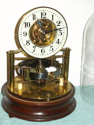 C.1912, English, Reason Mfg, Brighton, Electrically impulsed balance wheel clock, a skeleton layout on a mahogany base, under glass dome, made to the 1911 patent design of Thomas John Murday. — Antique Clocks Price Guide