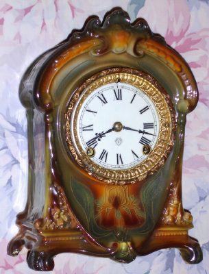 C.1910, Ansonia, Royal Bonn LA CRUZ, 8-day time and gong strike porcelain mantel clock, in New Art colors of very dark green accents of pastel rainbow colors and other highlights, and solid porcelain dial. — Antique Clocks Price Guide