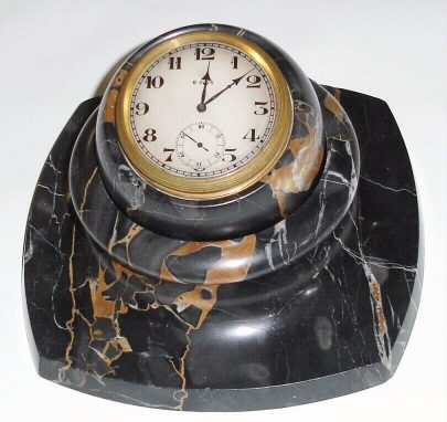 C.1930, Swiss, Gubelin, Gray marble desk clock, a jeweled rim wind clock, set into a variegated marble ball, which in turn sets into a matching recess in the marble base, so that it can be swiveled to any angle for viewing. Pull rim up for setting hands. — Antique Clocks Price Guide