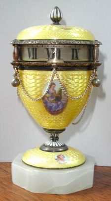 C.1890, Swiss/Austrian, Mini "Egg" on marble base, with a small stem wind 1-day movement, and with 6 mini cherubs in ovals applied to the yellow Guilloche enamel over silver. A 7th cameo below the indicator of a lady in a violet colored dress. — Antique Clocks Price Guide