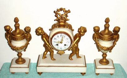 C.1890, French, 3-Piece Mantle Clock Set, of marble and white metal with gold patination, the clock being held by two cherubs and the garnitures each with a pair of winged cherubs. — Antique Clocks Price Guide