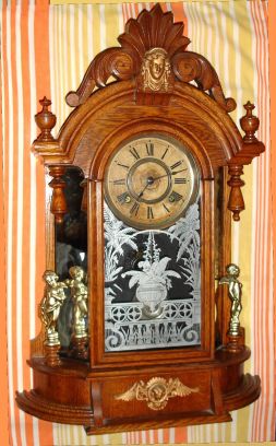 Ansonia Clock Company, Ansonia Conn. "TRIUMPH" model, 8-day brass time and strike mvt in oak mirror-sided case flanked by two cupids shelf clock, spring driven. C. 1880. — Antique Clocks Price Guide