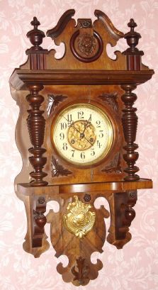 German, Junghans, Berlin style free swinger wall clock, walnut veneer, with matched embossed pendulum and dial center, 8-day time and gong strike. C.1905. — Antique Clocks Price Guide