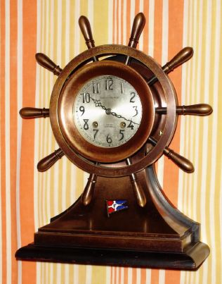 Chelsea Clock Co, Ship's Bell "YACHT WHEEL" model with 4 1/2" SPECIAL dial ( raised numerals), Model L movt, presentation piece contract for Black, Starr and Frost (on dial). Engraved along outer brass wheel "TO A GOOD SHIPMATE" + "F.C.E TO L.P.F" with fine multicolor enamel flag decorating base, spring driven, 8-day. C. 1926. — Antique Clocks Price Guide