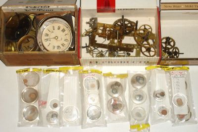 Box lot, best part of which is a carefully inventoried lot of 6-dozen new bulls eye watch crystals, glass, in various sizes, other items include a clock movement in pieces, minus its springs, and another large cigar box of dial plates and small novelty clock bezels. — Antique Clocks Price Guide