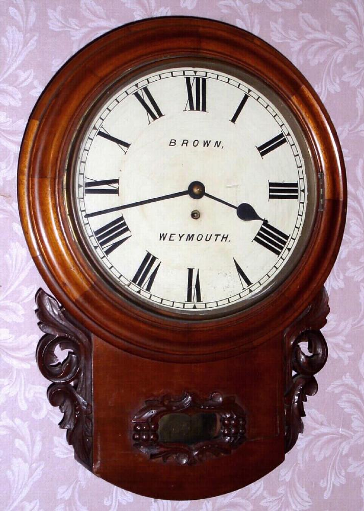 English, single train, chain fusee dial clock, C.1870, in a round top, short drop wall case of mahogany, 8-day with carved accents and a bottom door to access the pendulum, retailed by "Brown" of Weymouth. — Antique Clocks Price Guide
