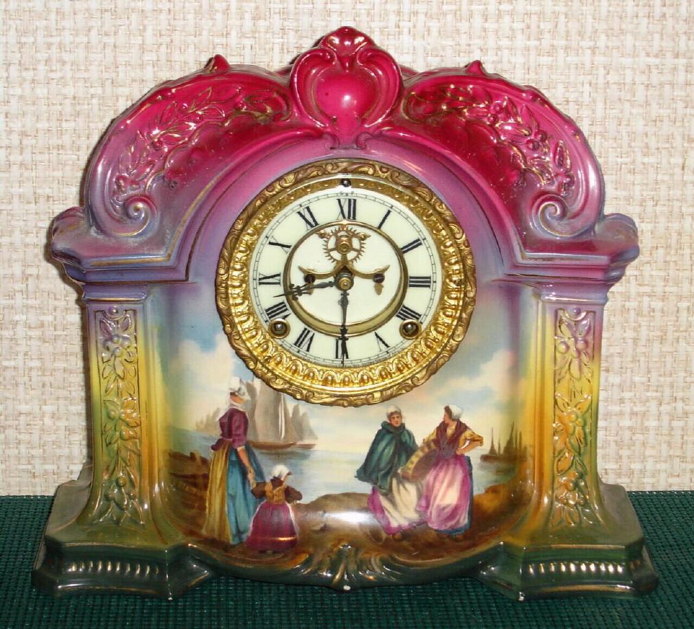 Ansonia Clock Co., C.1910, Royal Bonn, "LA ORB" porcelain china cased clock, with 8-day, gong strike mov't with open escapement on porcelain dial, in a multi-colored case, red top, yellow center + dark green at base, with multi colored floral decorations. Best part is the hand painted scene at bottom showing Dutch ladies saying farewell to their sailing husbands {ships in background}. — Antique Clocks Price Guide