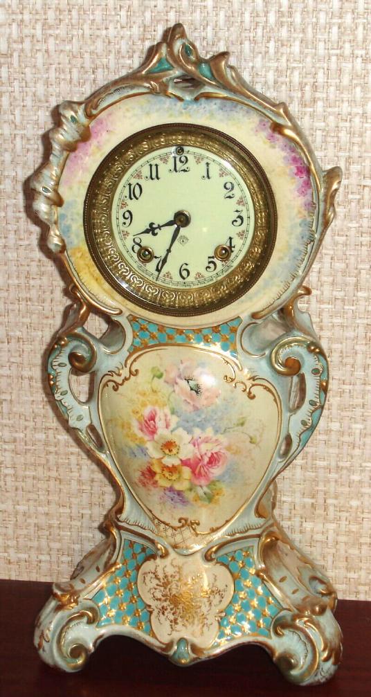 Ansonia Clock Co., Royal Bonn, "No. 506", slender porcelain clock in the French style, with flat porcelain dial, the white case with blue and aqua accents and gold highlights, and with a pink and magenta in the section below the dial, c.1900 — Antique Clocks Price Guide