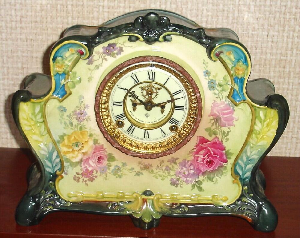 Ansonia Clock Co., C.1905, Royal Bonn, "LA RITA" porcelain china cased clock, with 8-day, gong strike mov't with open escapement on porcelain dial, in a multi-colored case, cream base, yellow and aqua accents to front, dark gray-green bottom and side trim, with varied color floral decorations. — Antique Clocks Price Guide