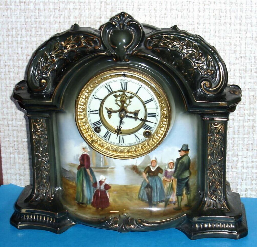Ansonia Clock Co., C.1905, Royal Bonn, "LA ORB" porcelain china cased clock, with 8-day, gong strike mov't with open escapement on porcelain dial, in a very dark green case [almost black], and with a painted scene below the dial showing a Dutch family at the harbor's edge bidding farewell to a sailor or fisherman. — Antique Clocks Price Guide