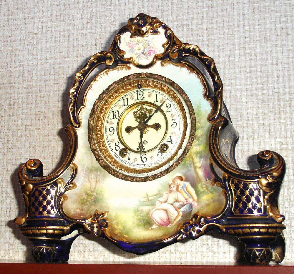 Ansonia Clock Co., C.1905, Royal Bonn, "LA VERA" porcelain china cased clock, with 8-day, gong strike mov't with open escapement on porcelain dial, in a cobalt blue case with 24K side decorations and portrait scene of lovers below the dial. — Antique Clocks Price Guide