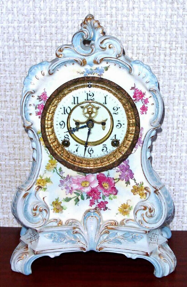 Ansonia Clock Co., C.1905, Royal Bonn, "LA CALLE" porcelain china cased clock, with 8-day, gong strike mov't with open escapement on porcelain dial, in a white china case with light blue accents and gold highlights, the case decorated with yellow and magenta flowers. — Antique Clocks Price Guide