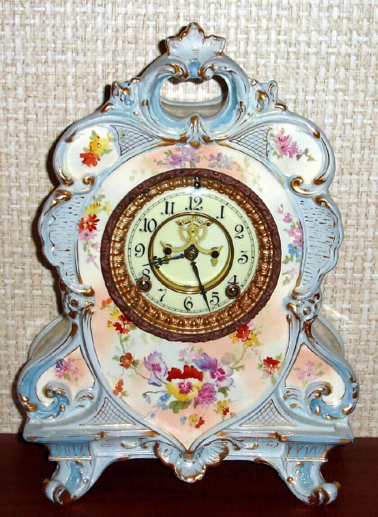 Ansonia Clock Co., C.1905, Royal Bonn, "No. 504" porcelain china cased clock, with 8-day, gong strike mov't with open escapement on porcelain dial, in a white china case with light blue accents and pale pink and gold highlights, the case decorated with magenta flowers. — Antique Clocks Price Guide