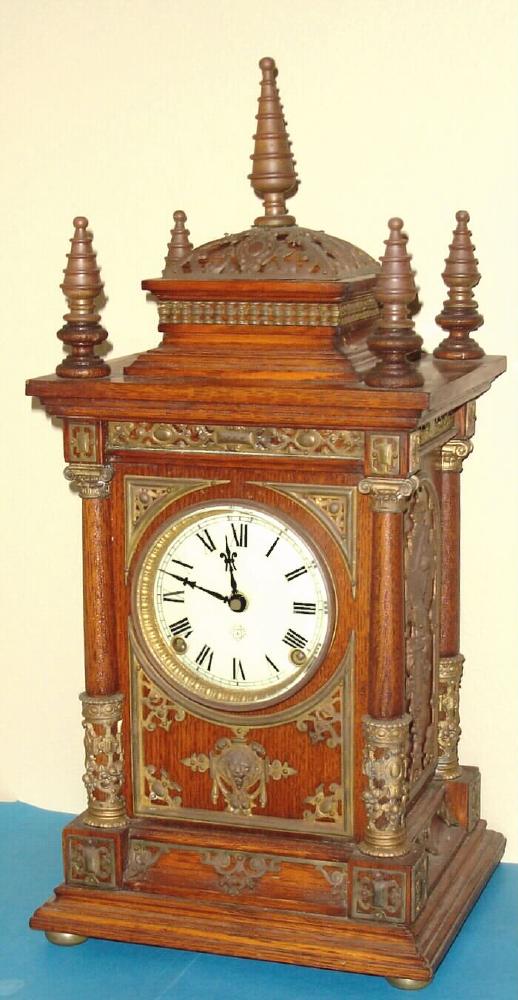 Ansonia Clock Co., C.1894, "CABINET ANTIQUE", oak cased mantel clock with brass trimmings, this one with one piece porcelain dial. Note variations in movement between this one and lot with fancy dial. This one has low mount iron based gong, as used in many mantle models. — Antique Clocks Price Guide