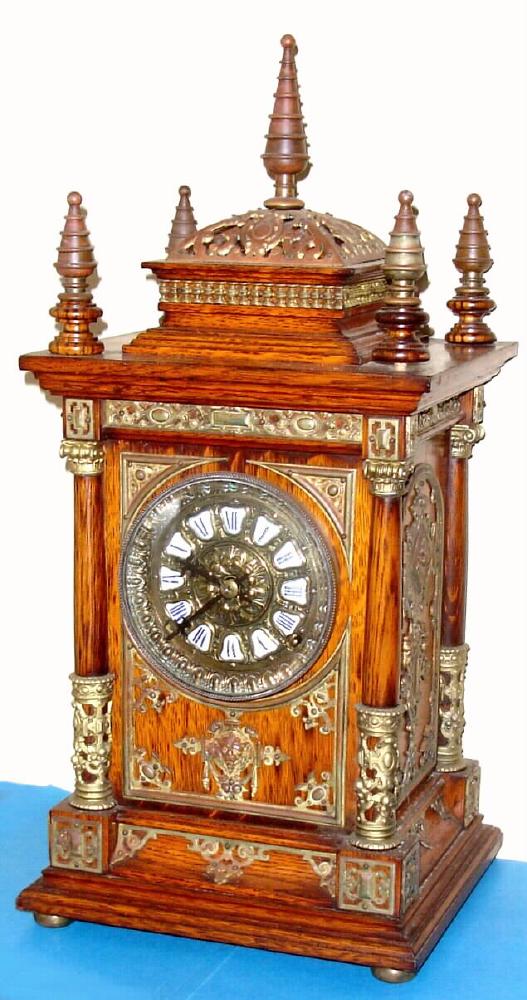 Ansonia Clock Co., C.1894, "CABINET ANTIQUE", oak cased mantel clock with brass trimmings, this one with one with fancy dial, w/ individual porcelain cartouche numerals.. Note variations in movement between this one and lot with plain dial. This one has fancy embossed plates and cups protecting the springs, plus tall gong standard. — Antique Clocks Price Guide