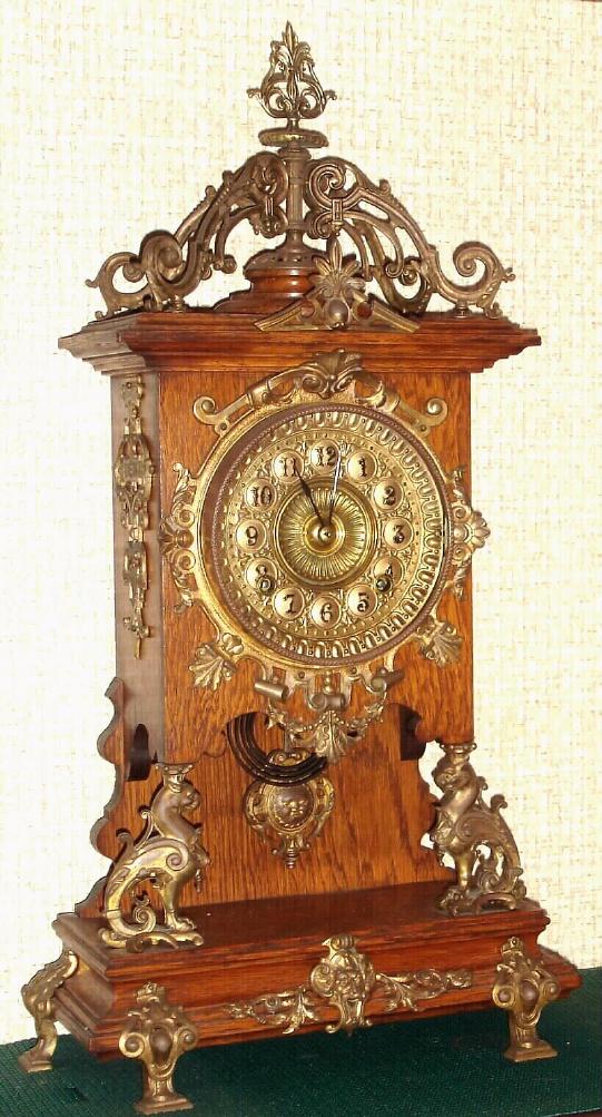 Ansonia Clock Co., New York, "CABINET - D" antique oak finished mantel clock with brass trimmings, this model with "open well" design to show the fancy cast pendulum w/ sun burst face in center. Fancy brass dial is embossed with numerals on raised circles, c.1894 — Antique Clocks Price Guide