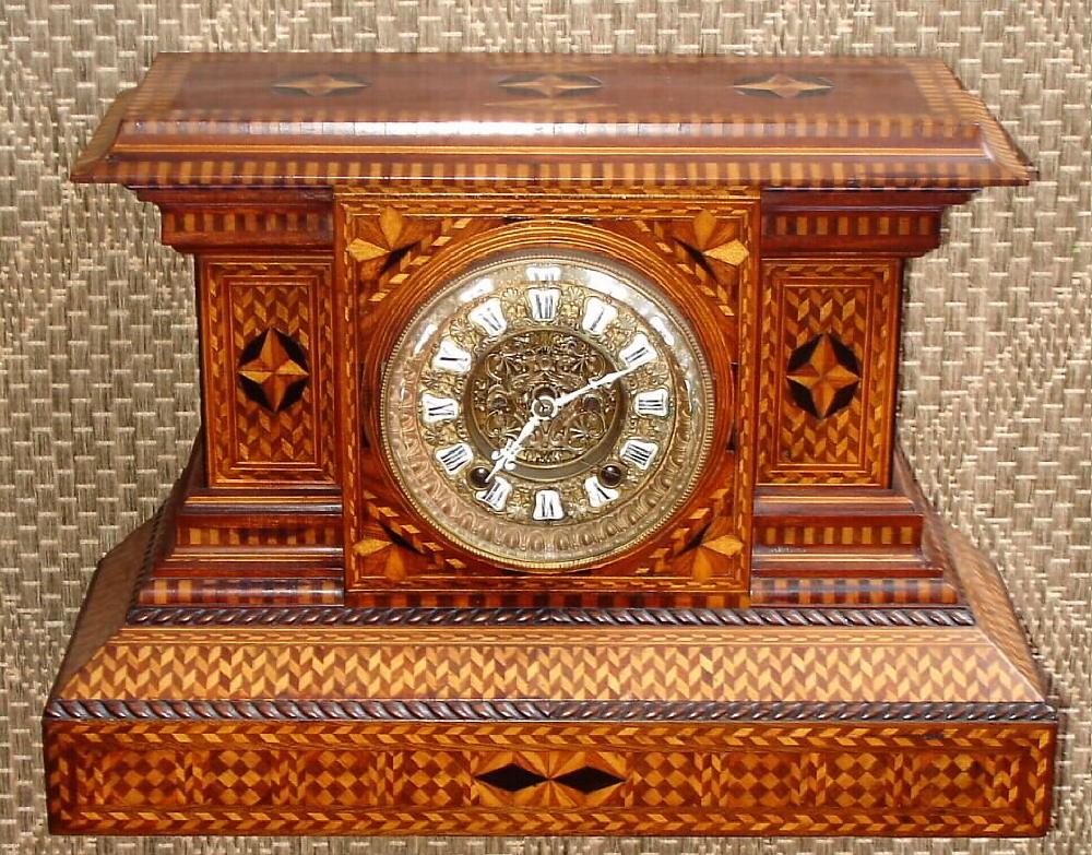 Ansonia Clock Co., New York, movement in a custom made parquetry case with the finest hounds tooth detail. 8-day, strike, C.1900. Note this movement is Ansonia's best round French style with rack striking and fancy brass dial with cartouche numerals and open escapement with eagle head support for top pivot. — Antique Clocks Price Guide