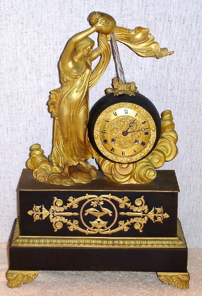 French, Waterfall Automaton, C.1860, with a small bell strike movement with early cylinder platform. The twisty glass tube simulates water pouring from the maidens jug above the clock. The automaton is a separate movement in the base of the clock, wound from the right side. — Antique Clocks Price Guide