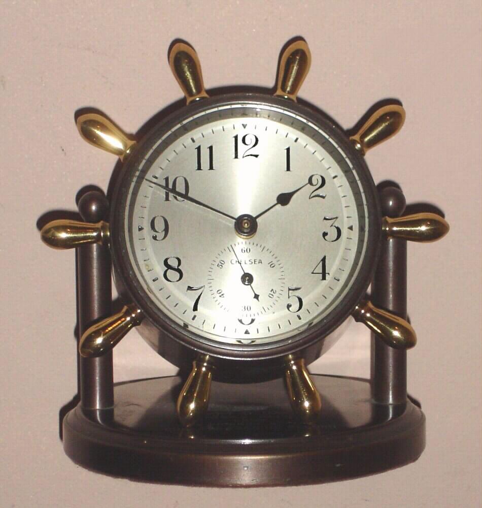 Chelsea Clock Co., Boston, C.1949, CLINTON model desk clock with 2 3/4 inch dial, and tu-tone case with bronze base and tub with yellow brass handles. This model was first introduced in 1931. 8-day, time. A presentation piece, engraved on the base to "Herbert D. Hancock, 1924-1949, from his friends at the CHELSEA EVENING RECORD" [newspaper] — Antique Clocks Price Guide