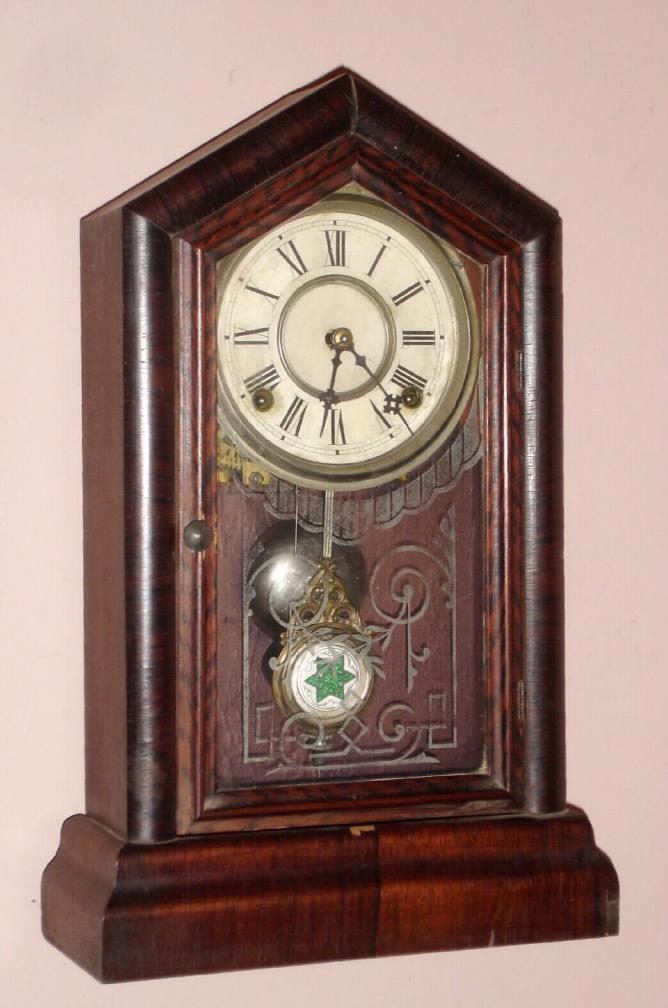 New Haven Clock Co., "GEM EXTRA", 8-day time and gong strike mantel clock in a Gothic case with rosewood veneer, and with pressed glass pattern pendulum. — Antique Clocks Price Guide