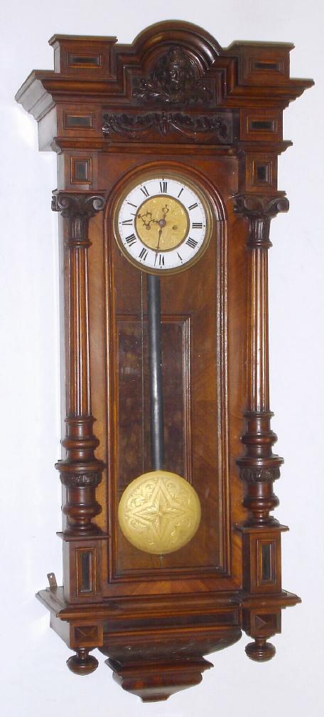 Austrian, Gebruder Resch (Remember), smaller 2-wt, with 5.5" dial, as-found, LESS weights and pulleys. Has rod strike. Walnut case has robust 3/4 columns with heavily carved capitals and a nice carved head in the "built in" top, plus carving on the base. — Antique Clocks Price Guide
