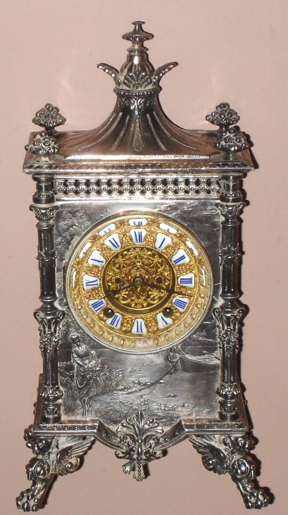 Ansonia Clock Co., "ELITE", cast metal mantel clock, finished in nickel-silver, and with Ansonia's fanciest visible escapement, the 'scape wheel supported by two winged griffins, and the Roman numerals on individual porcelain cartouches, c.1904 — Antique Clocks Price Guide