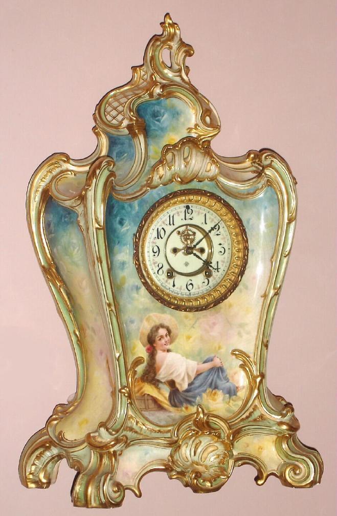 Ansonia Clock Co., NY, Royal Bonn, rare "LA PROVENCE", porcelain cased mantel clock with open escapement and signed portrait below the dial, the largest and most beautiful clock made by Ansonia. 8-day, gong strike. Fancy dial with red tre-foils between the numerals, c.1908 — Antique Clocks Price Guide