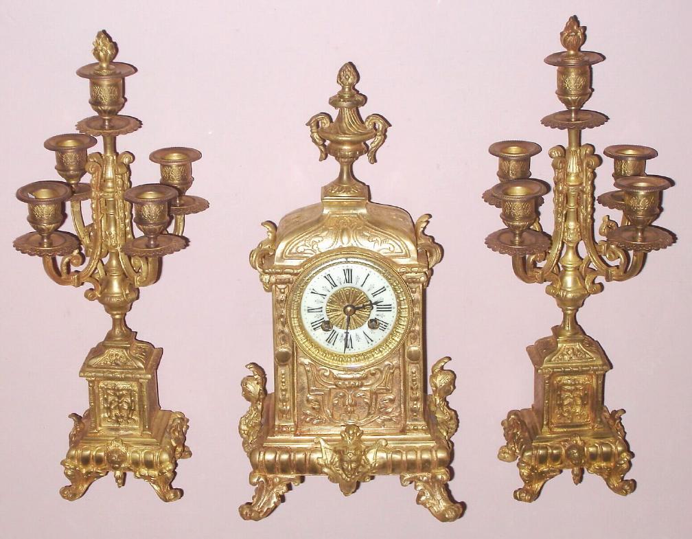 French, C.1880, 3-piece mantle set of brass, cast with scrolls and pilasters and busts on the base, both sides and center. The matching candle stands have 5 lights each, and with cherub busts on the bases. — Antique Clocks Price Guide