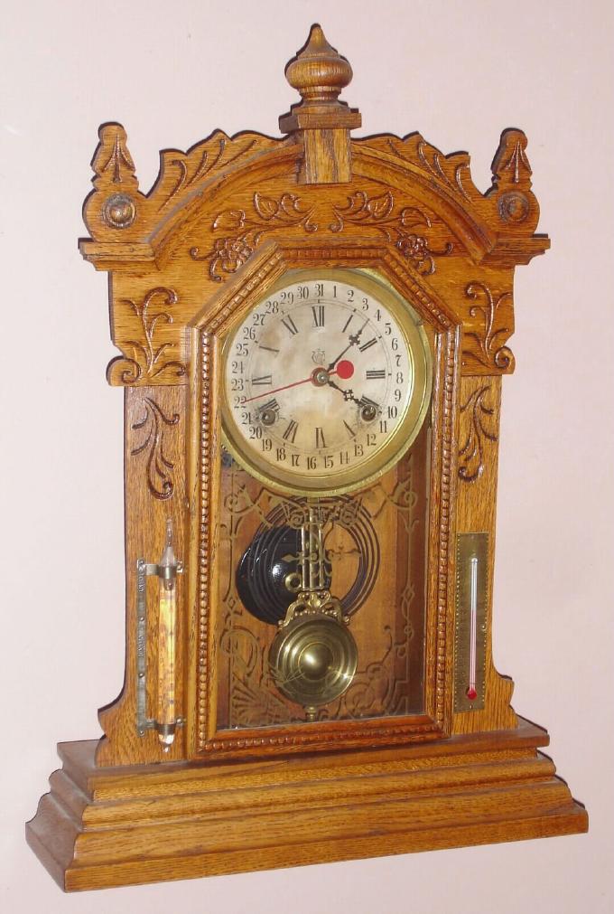 Waterbury Clock Co., pressed oak gingerbread clock with central calendar, time and gong strike, 8-day. Also with thermometer and weather tube intact, c.1900. — Antique Clocks Price Guide