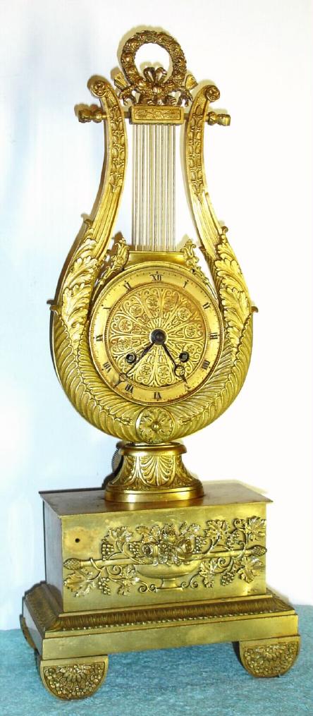 French, Lyre Form mantel clock, c.1830, silk thread suspension, in an ormolu lyre frame with gilt brass base. The mov't with rear adjust for F/S. Gilt dial with painted Roman numerals. — Antique Clocks Price Guide