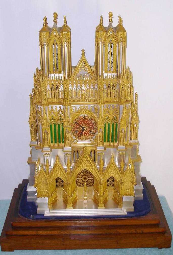 French, Raingo Frs, Paris, bronze, silvered brass and ormolu clock in the form of Reims Cathedral, c.1850. Cathedral of Our Lady in the City of Reims, stands in the Champagne-Ardennes region of France, and is considered one of the finest examples of the High Gothic style of architecture. The kings of France were once crowned in Reims Cathedral. Note that dozens of little cast and chased 'Saints' line the windows, exactly as the real building. Clock sets on its original rosewood base, and with a glass cover/ 5 panes in a wooden frame. Well made silk thread movement is signed as above. — Antique Clocks Price Guide
