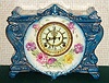 Ansonia Clock Co., C.1900, Royal Bonn, "LA VINDA" porcelain china cased clock, with 8-day, gong strike mov't with open escapement on porcelain dial. Case is dark aqua with fields of cream decorated with magenta and yellow flowers.