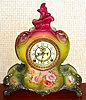 Ansonia Clock Co., C.1905, Royal Bonn, "LA VENDEE" porcelain china cased clock, with 8-day, gong strike mov't with open escapement on porcelain dial, in a tri-colored case, red top, lime-yellow center + dark green at base, with multi colored floral decorations on the lower front and sides.