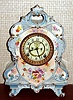 Ansonia Clock Co., C.1905, Royal Bonn, "No. 504" porcelain china cased clock, with 8-day, gong strike mov't with open escapement on porcelain dial, in a white china case with light blue accents and pale pink and gold highlights, the case decorated with magenta flowers.
