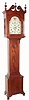 A reproduction tiger maple tall clock with scroll top and carved rosettes, full columns flanking the hood door, and quarter columns flanking the tombstone door with carved fan at top. The base or plinth of the case has matching quarter columns and well proportioned French feet. With a period [C.1830] American 8-day 2-wt time and strike movement, having a painted iron dial with Roman numerals and eagle in the arch.