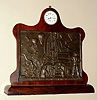 Desk clock on walnut stand with quality Swiss fully jeweled stem wind pendant set one day watch movement with 24 hour Arabic numeral porcelain dial set in scrolled top above bronze plaque in Diego Rivera style depicting factory scenes commemorating the opening of the H.D.A. factory in Redditch, England in 1939, c1940