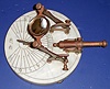 George Dorne, New York, No. 2, Circa 1973, Noon cannon. This is a copy based on a French style that was popular in the 18th century. The magnifying glass if set properly would concentrate the light to fire the loaded cannon at 12 o'clock. The setting angle of the magnifying glass can be set depending on the season to make it operate. The longitude and latitude are indicated on the marble base plate.