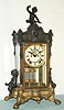 Ansonia Clock Co., 4-Glass crystal regulator, PEERLESS, with 3 figures, Cupid at top [with arrow still attached], and the case flanked by 2 other cherubs, open escapement on the dial and gong striking, C.1905