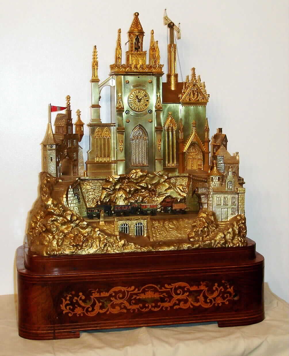 French, Napoleon III, ormolu musical and automaton novelty mantel clock, in the form of a castle, time and bell strike with silk thread suspension, c.1870, less dome, two "trains" with early style locomotives and cars traveling across the front on two bands, driven by an independent spring barrel, the plinth also housing a musical movement — Antique Clocks Price Guide