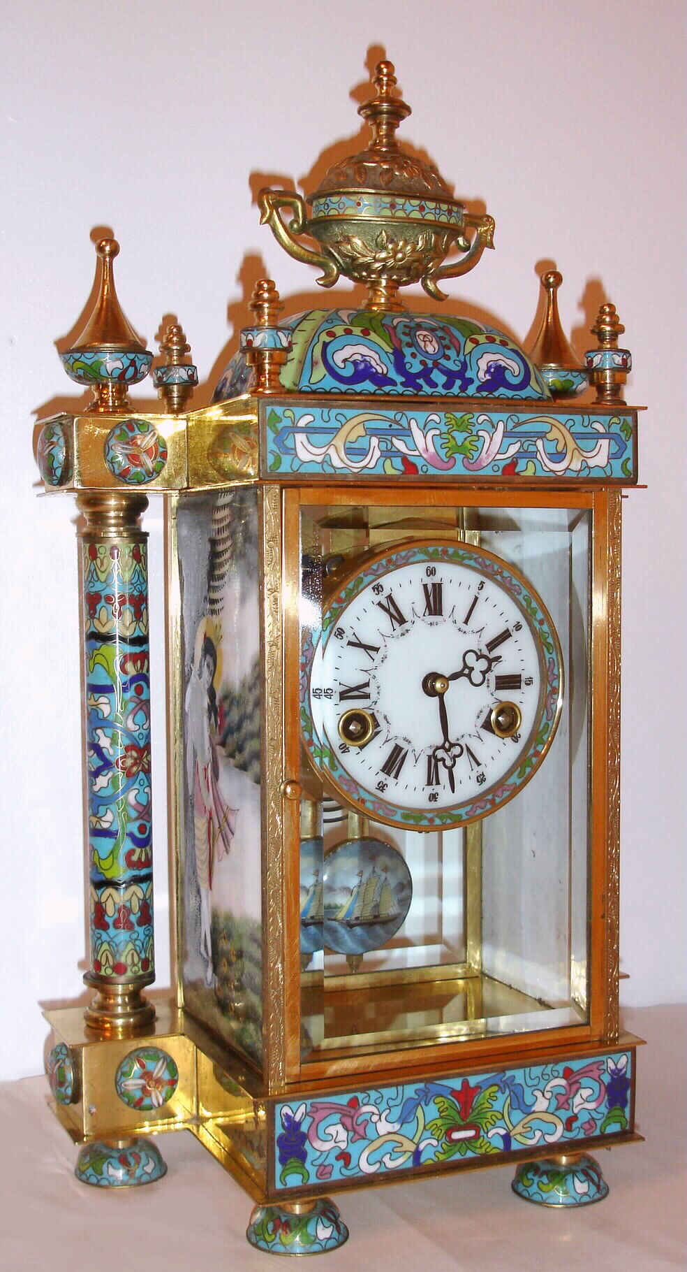 Chinese, (modern) 8-day time/strike brass and enamel crystal regulator, larger model with free standing columns at each side and urn top. Side panels depicting Asian dancers in costume, a sailing ship on the pendulum, C. 1990 — Antique Clocks Price Guide