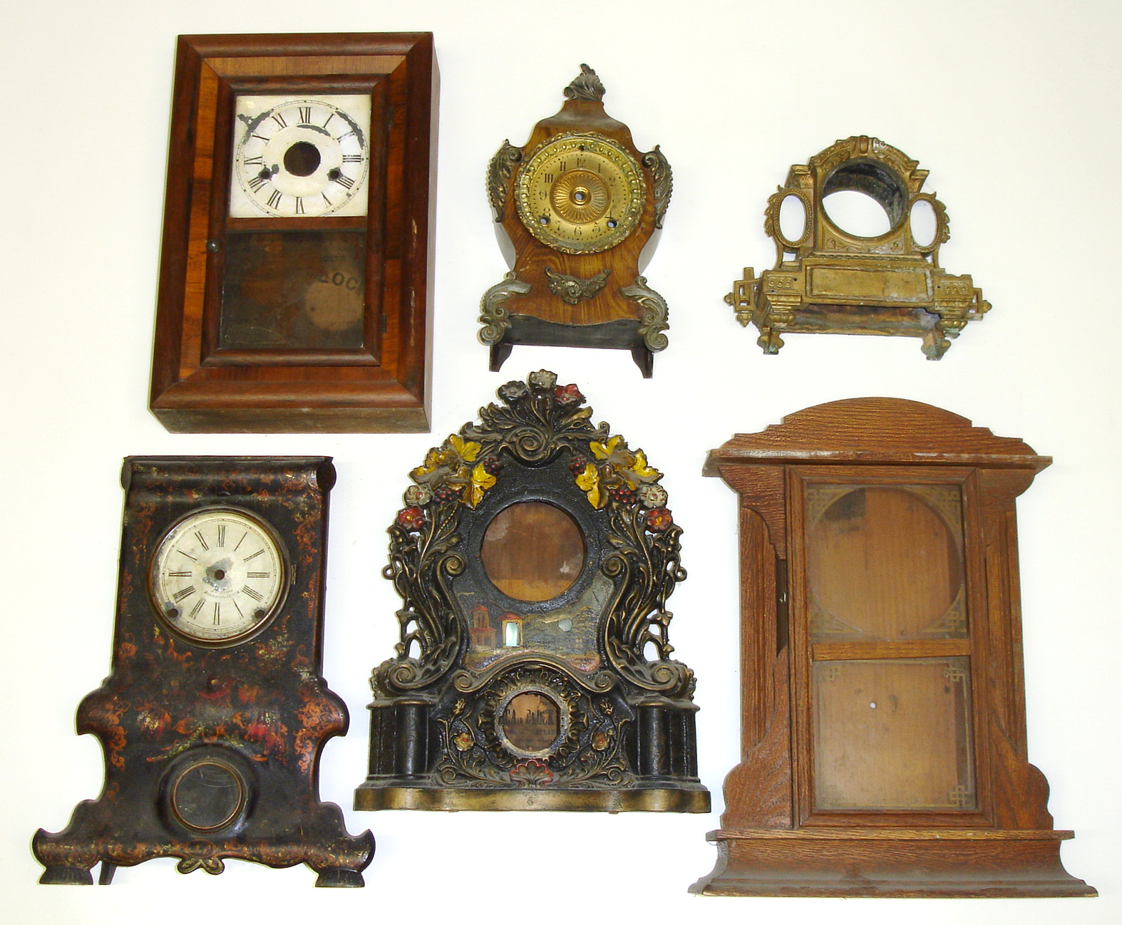 Six clock cases; one miniature ogee, one kitchen clock, two iron fronts (one with J.C. Brown dial), two fancy cast-metal. Largest is 19" tall — Antique Clocks Price Guide
