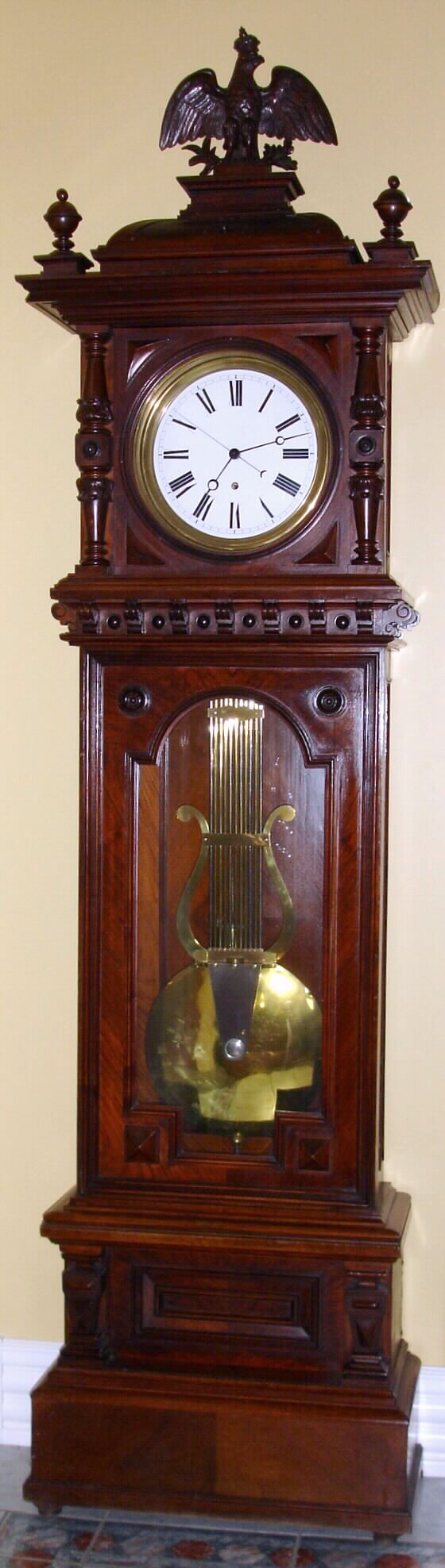German "Alt Deutsch" style tall case with later Swiss pinwheel escapement movement and high grade grid iron pendulum. The case is mahogany with carvings and turnings and surmounted by carved crowned eagle finial. The porcelain enamel dial has sweep seconds, c1880 — Antique Clocks Price Guide